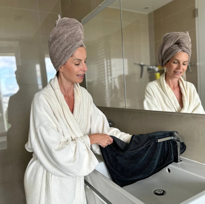 Woman in bathrobe and towel on head drying a chrome tap